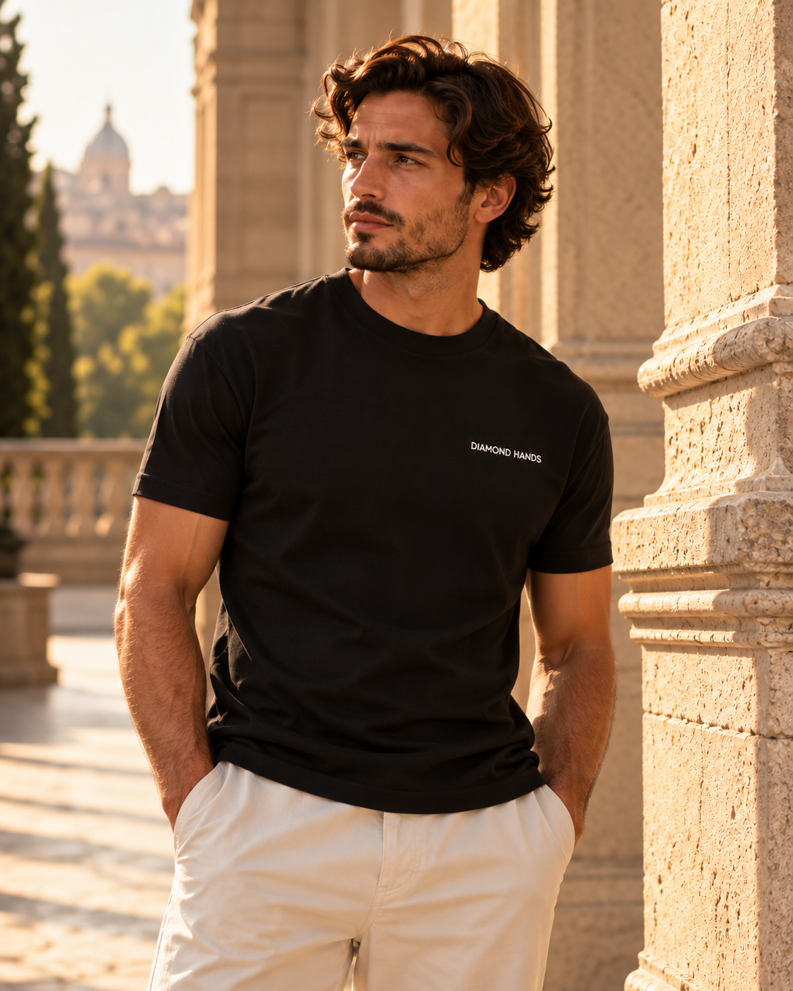 Man wearing a black Diamond Hands T-shirt with white left-chest embroidery beside sunlit stone columns.